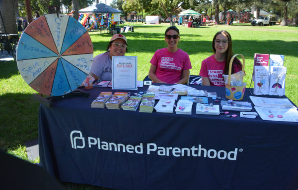 Three Planned Parenthood staffers sit at a table with their organization's name on the tablecloth at SGV Pride 2019