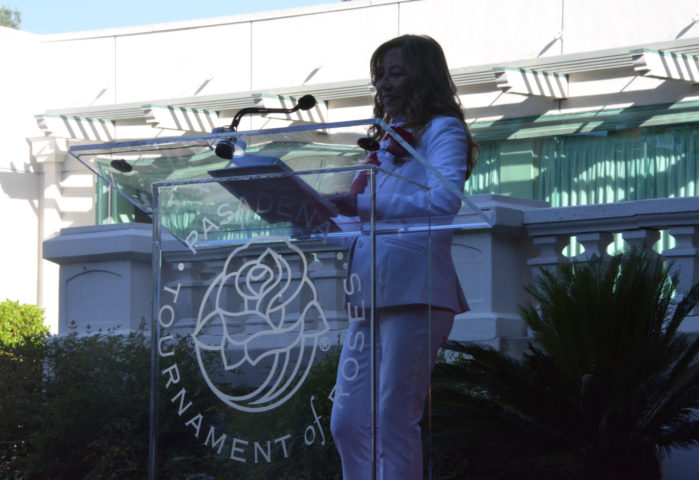 Ruth Martinez-Baenen reads from notes as she stands at translucent lectern with "Pasadena Tournament of Roses" and rose logo