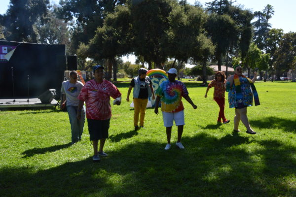 Reverend KC demonstrates a kick while line dancing with five attendees at San Gabriel Valley Pride 2019