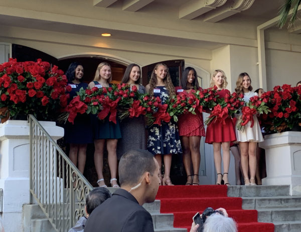 Seven members of the 2020 Royal Court smile from the doorway of Tournament House as they hold rose bouquets