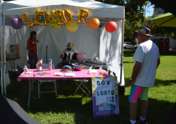 Singer in a red shirt with headphones at a tent with "SENIOR" over it in gold balloons