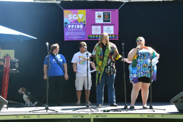 Reverend Pat extends her hands in prayer as Reverend KC speaks and other leaders look on onstage at San Gabriel Valley Pride