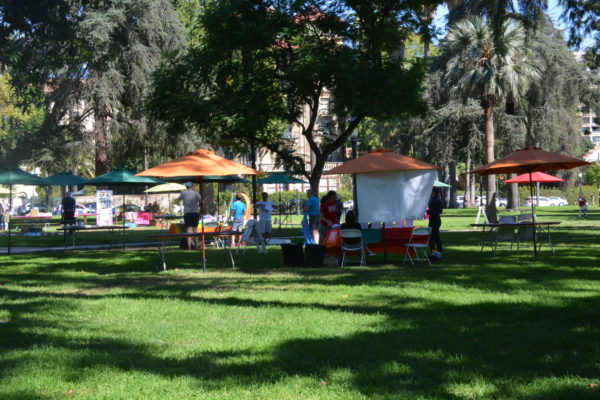Volunteers begin decorating tables under rainbow-colored umbrellas in Pasadena's Central Park prior to SGV Pride Festival 2019