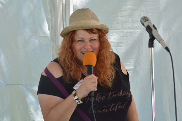 Redhaired woman with fedora smiles as she sings into mic
