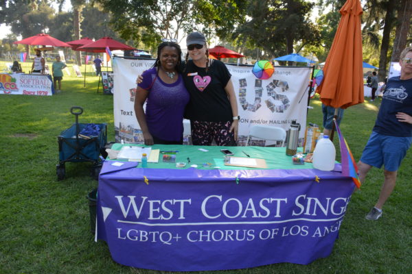 Two staffers smile at West Coast Singers table with purple tablecloth and literature