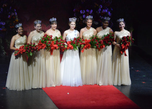 Rose Queen® Camille Kennedy and her Royal Court stand onstage holding red roses