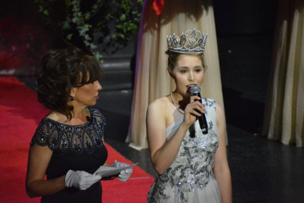 Rose Queen® Camille Kennedy speaks into microphone as Tournament of Roses® President Laura Farber reads the words from a sheet