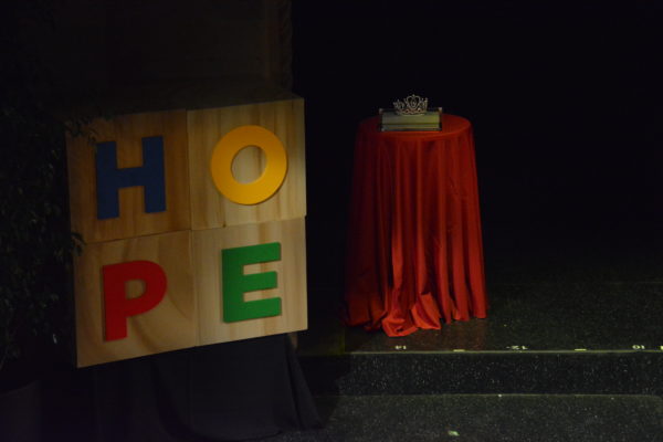 Jeweled crown sits on table near a block with "HOPE" on it, at Rose Queen® coronation program