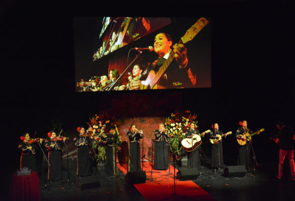 Nine-piece Mariachi Divas ensemble onstage, led by their music director, with overhead screen broadcasting their performance during Rose Queen® coronation program
