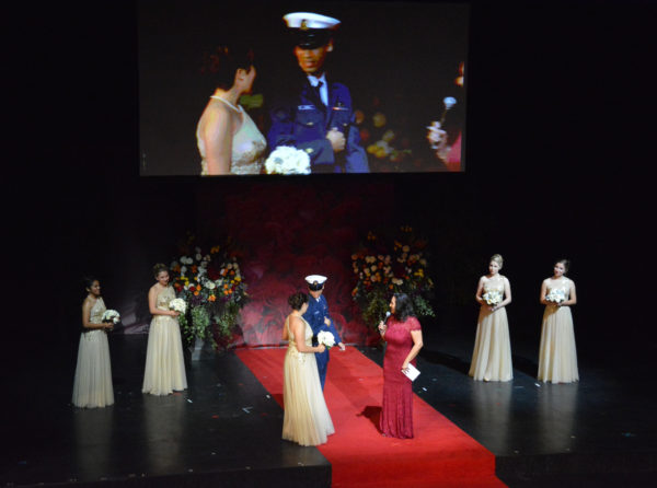 Lynette Romero stands among Royal Court princesses onstage as Emilie Risha comes out on the arm of an escort at Rose Queen® coronation ceremony