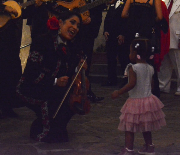 Mariachi Divas singer smiles as she crouches down to sing to thrre-year-old