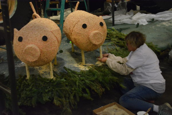 Volunteer attaches dried materials to two barrel-sized pink porcine structures on the Chipotle float