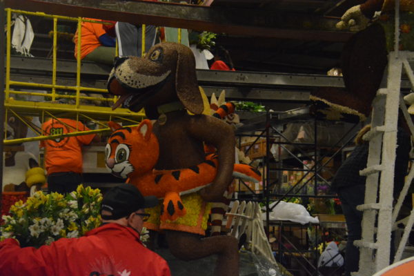 Two red-coated Fiesta staffers glue materials on the figure of a long-eared hound with an inner tube shaped like a smiling cat