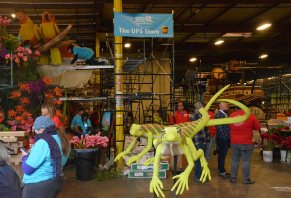 volunteer works on UPS Store float next to two standing geckos and a "UPS Store" banner