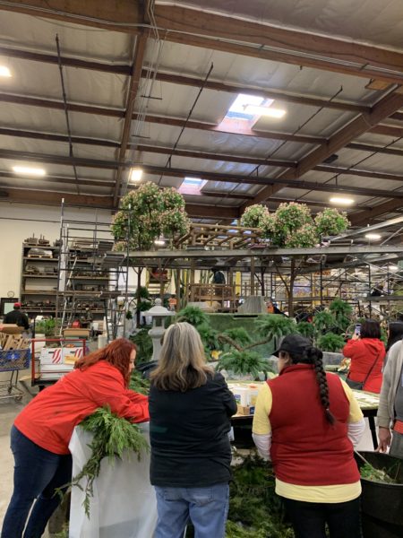 Two Fiesta staffers, in bright red jackets, work with two volunteers placing greenery on the Torrance float