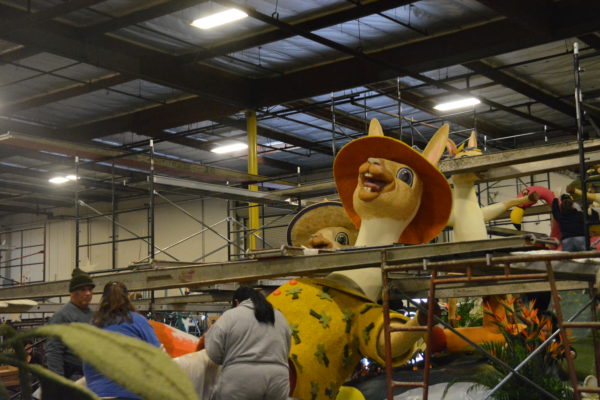 Volunteers decorate a float featuring two outsized river rafting llamas with big grins and straw hats