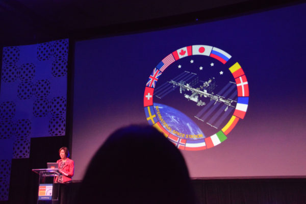 Dr. Ellen Ochoa with graphic of ISS surrounded by flags of the world at California STEAM Symposium