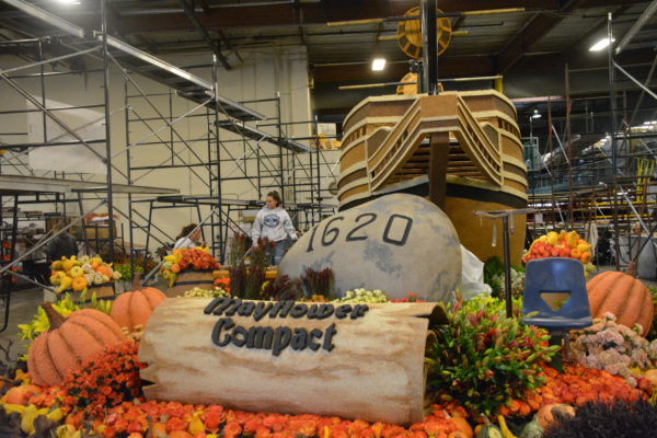 Mayflower ship model with "Mayflower Compact" on the rock before it as it lands and crops including pumpkins on the shores