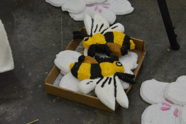 Bee cutouts with yellow-and-black dried-material stripes lie in a box ready to be put on the float