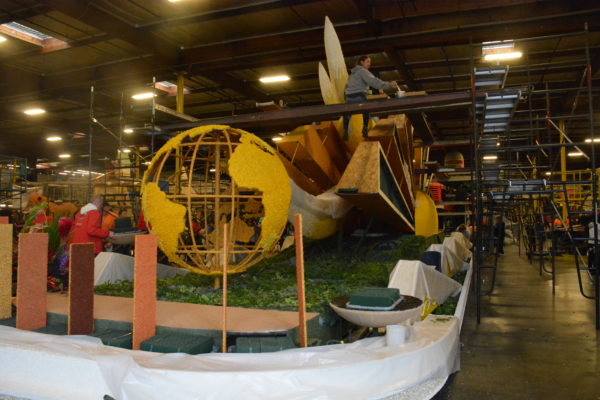 Fiesta Parade Floats staffer stands on float with a giant globe, attaching dry materials