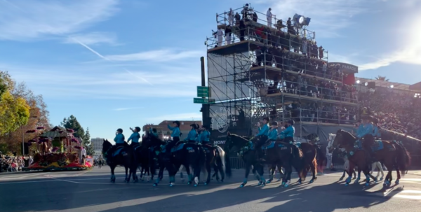 Blue Shadows Mounted Drill Team equestrians ride horses with glittery blue covering on their hooves past the reviewing stand