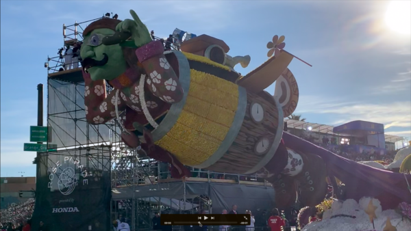 Trader Joe's "Fearless Flyer", with goggles and flight helmet, soars from the front of a float in a pickle barrel