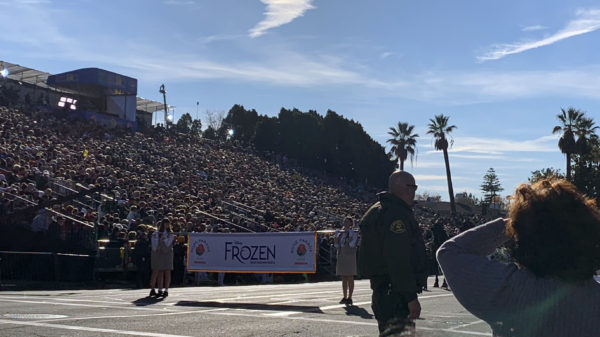 Two marchers hold Frozen banner as onlookers crane to see the show