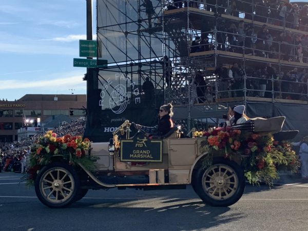 Gymnast Laurie Hernandez waves from the back seat of a model T