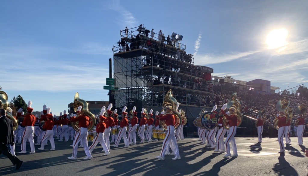 Pasadena City College Honor Band, in red jackets and white slacks, march past the reviewing stand playing trumpets and drums