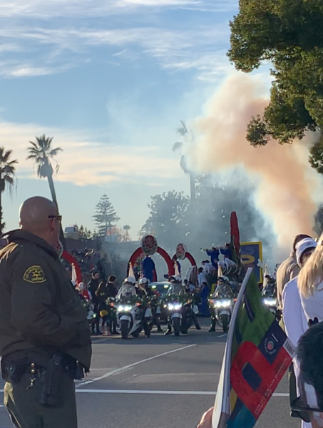 Police motorcycles flash their lights as pink smoke rises from the performance stage during Rose Parade pre show performance