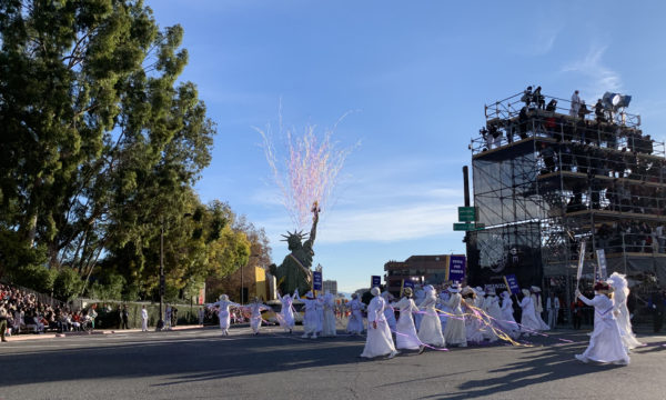 Pink streamers fly into the sky from Statue of Libery aboard Pasadena Celebrates 2020 float, as women costumed in white suffragette outfits follow with signs on sticks