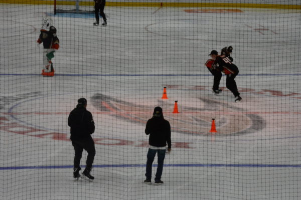Player in orange grapples with player in white near cones with pucks atop them