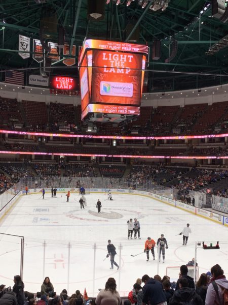 First Flight Field Trip elementary students pack Honda Center as Anaheim Ducks skate on the ice with "Light the Lamp" and "Welcome First Flight Field Trip" on a red four-sided lantern hanging above the center of the rink