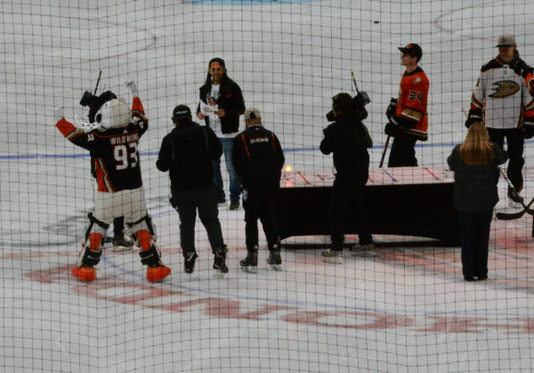 Wild Wing raises both arms in celebration and Sammy looks on with ccamera crew on ice as lamp glows red