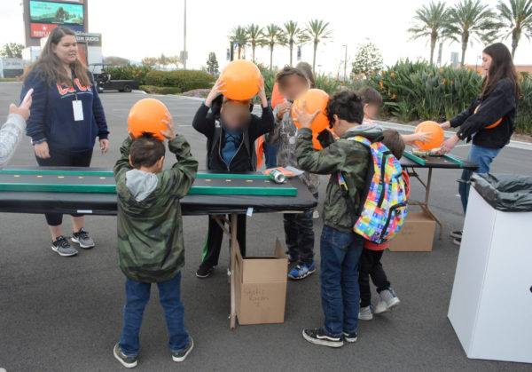 Three elementary-school boys rub orange balloons against their hair near "racetrack" with soda cans waiting