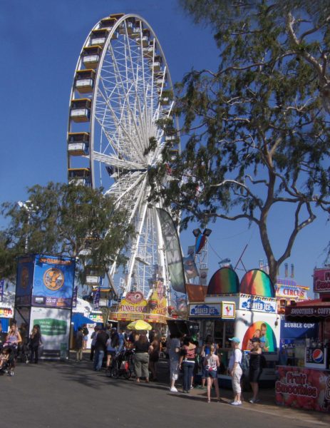 Ferris wheel and fairgoers on OC Fair main drag against blue sky
