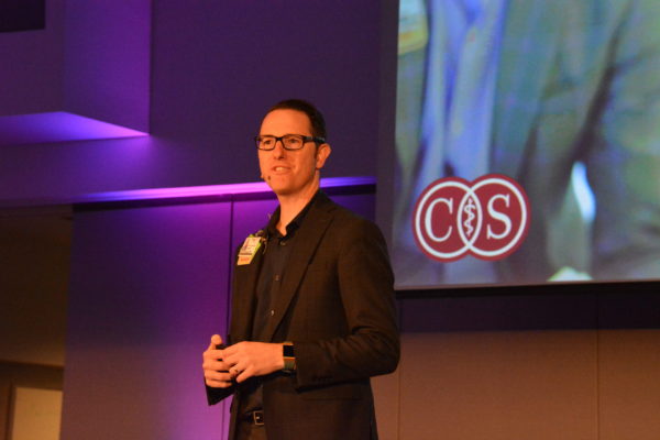 Dr Brennan Spiegel onstage with "C-S', for "Cedars-Sinai", on a slide behind him