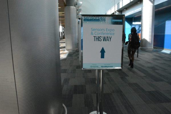 Attendee walks past sign with arrow and "Sensors Expo and Conference, this way"