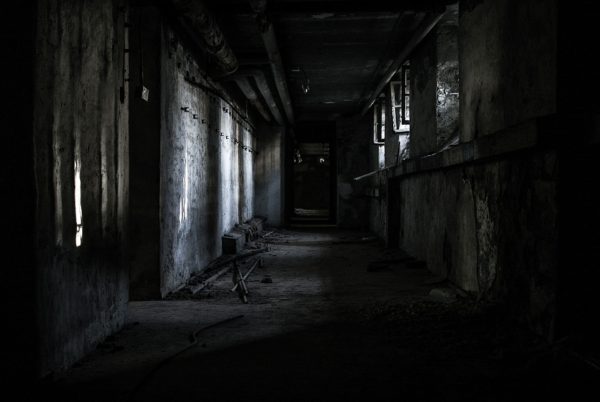 Creepy black-and-white depiction of an alley at night with lights from upper windows shining in weird patterns on opposite brick wall