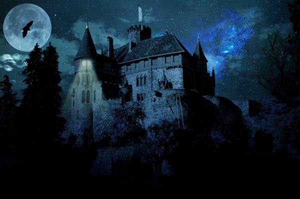 Lone bat flies across a full moon near a creapy castle silhoutted against a blue-black sky