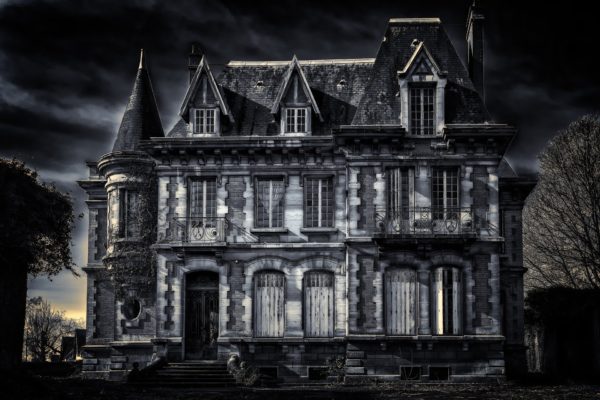 A creepy Gothic villa, depicted in black and white, stands against a cloudy, dark night sky