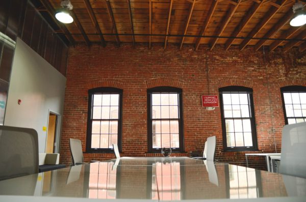 Conference table in brick-walled room with three windows and empty chairs