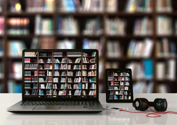 Laptop computer reflects shelf of books in library next to iPhone on desk