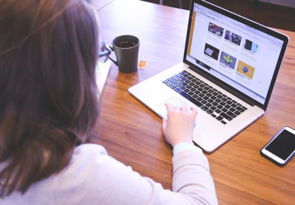 Woman sits at notebook computer with cup of coffee nearby at wooden desk