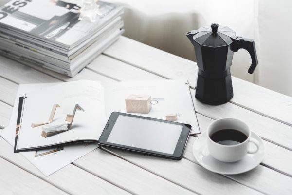 Coffee pot and coffee cup near tablet computer and books on white wooden outdoor table
