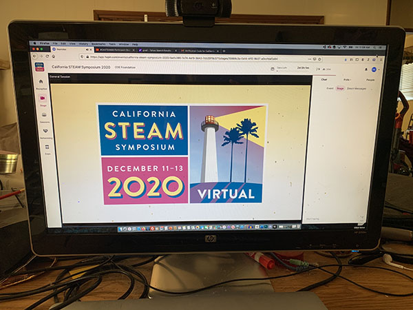 California STEAM Symposium logo shows lighthouse with beam of light under a palm tree, displayed on a notebook computer atop a desk