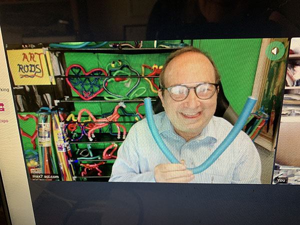 Max Schafer smiles on Zoom screen as he exhibits a light-up neon art rod in the background of his Art Rods display