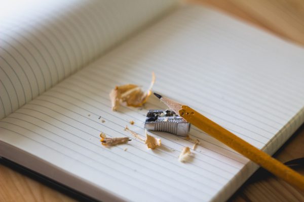 A sharpened pencil with pencil shavings and sharpened rests on an empty lined notebook page