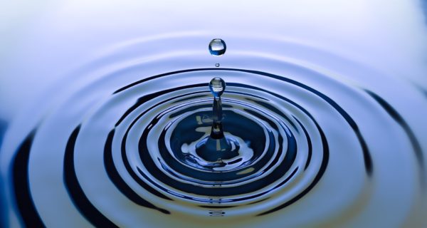 Water drop splashes up and causes outward circle of ripples