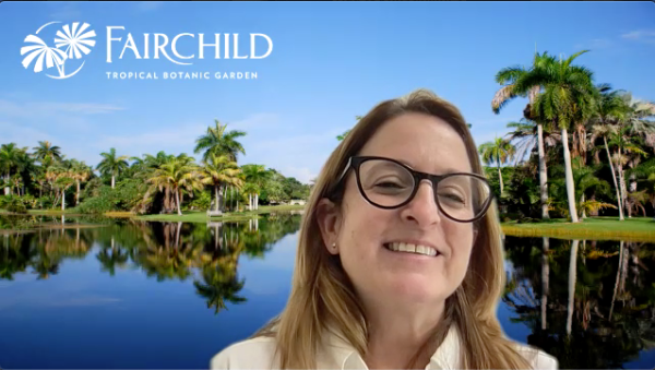 Fairchild Director of Education Amy Padolf smiles against a background of blue water and palm trees with "Fairchild Tropical Botanic Garden" in white lettering, while discussing the "Growing Beyond Earth" project.